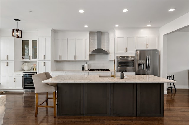 kitchen with stainless steel appliances, wall chimney range hood, a kitchen island with sink, beverage cooler, and dark hardwood / wood-style flooring