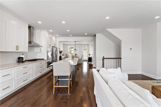 kitchen with wall chimney range hood, white cabinetry, dark hardwood / wood-style flooring, and a kitchen breakfast bar