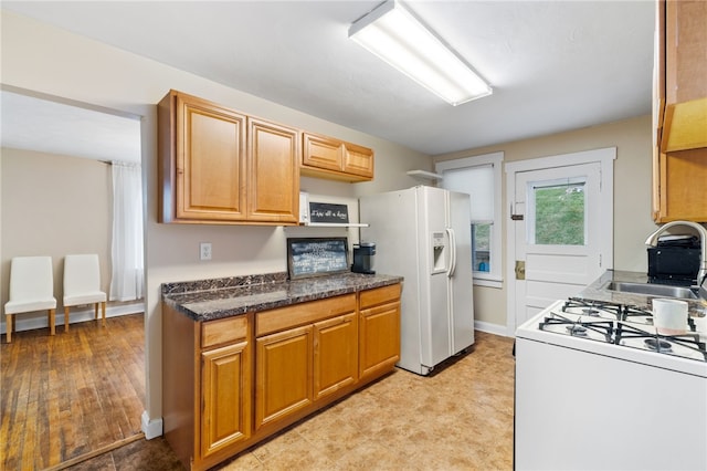 kitchen featuring sink, white appliances, and dark stone counters