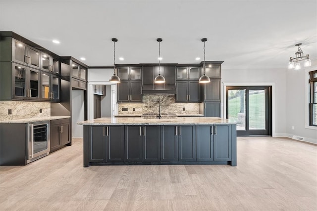 kitchen featuring light stone counters, hanging light fixtures, beverage cooler, and custom range hood