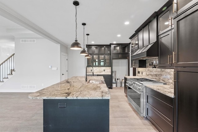 kitchen with light wood-type flooring, tasteful backsplash, high end stove, a spacious island, and sink