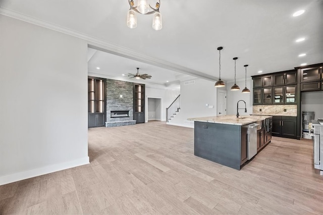 kitchen with decorative light fixtures, dark brown cabinets, a center island with sink, ceiling fan with notable chandelier, and light wood-type flooring