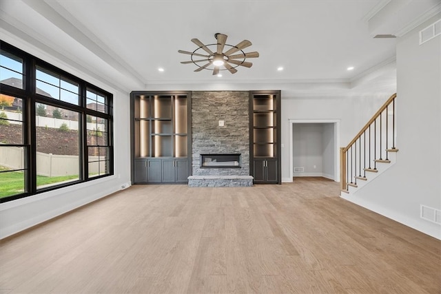 unfurnished living room with ornamental molding, light wood-type flooring, a stone fireplace, and a healthy amount of sunlight