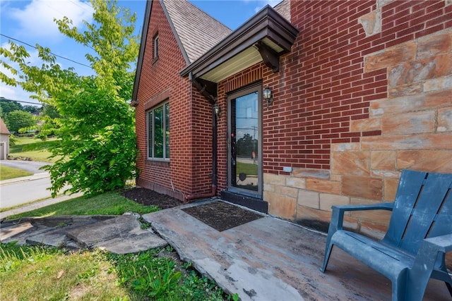 entrance to property featuring brick siding and roof with shingles