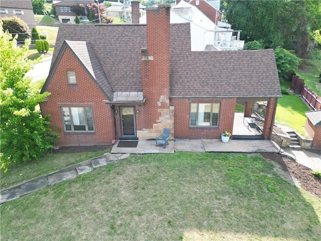 view of front facade featuring brick siding, a patio, a chimney, a shingled roof, and a front yard