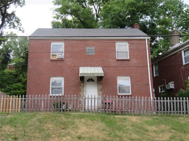 colonial inspired home featuring a wall unit AC and a front lawn