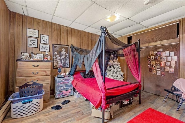 bedroom featuring wood-type flooring, a drop ceiling, and wooden walls