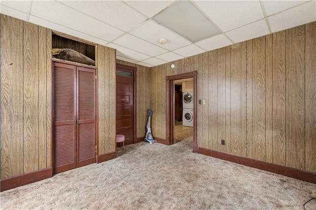 spare room featuring a drop ceiling, stacked washer / drying machine, wood walls, and carpet flooring