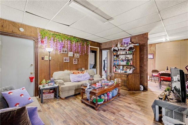 living room featuring light hardwood / wood-style floors, a drop ceiling, and wooden walls