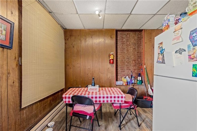 dining area featuring a paneled ceiling, wooden walls, and hardwood / wood-style floors