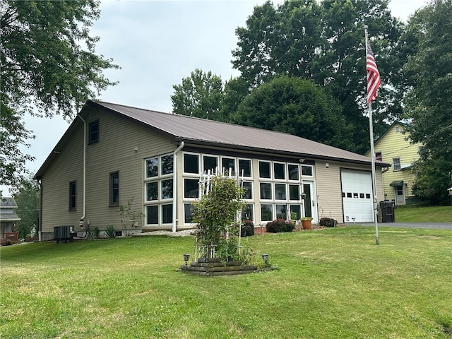 back of house with central air condition unit, a garage, and a lawn