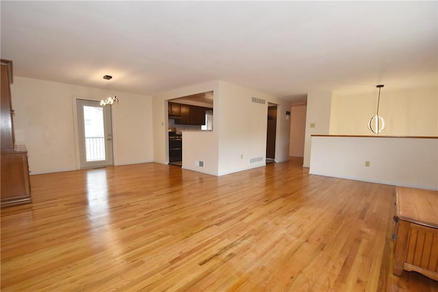 unfurnished living room featuring an inviting chandelier and light hardwood / wood-style flooring