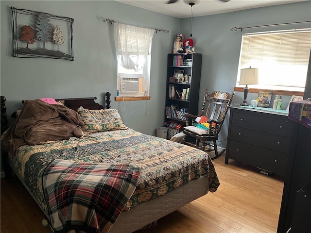 bedroom with cooling unit, light hardwood / wood-style flooring, multiple windows, and ceiling fan