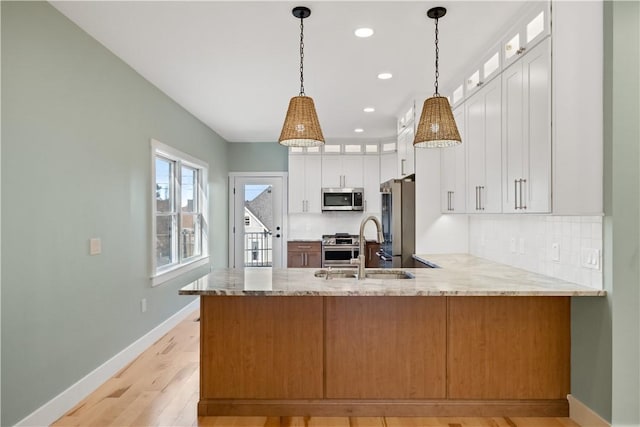 kitchen with white cabinetry, kitchen peninsula, stainless steel appliances, light stone counters, and sink