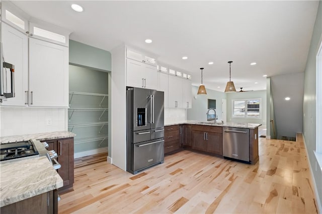 kitchen featuring white cabinetry, stainless steel appliances, pendant lighting, light stone counters, and sink