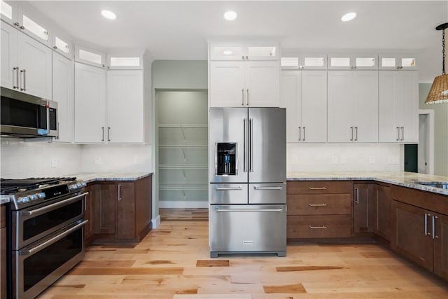 kitchen with appliances with stainless steel finishes, pendant lighting, white cabinetry, and light stone countertops