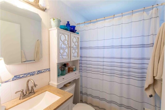 bathroom with tile walls, tasteful backsplash, toilet, and vanity