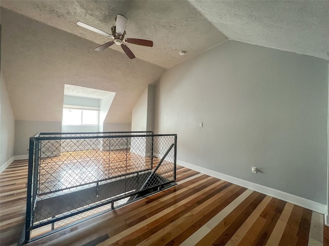 additional living space featuring a textured ceiling, ceiling fan, wood-type flooring, and vaulted ceiling