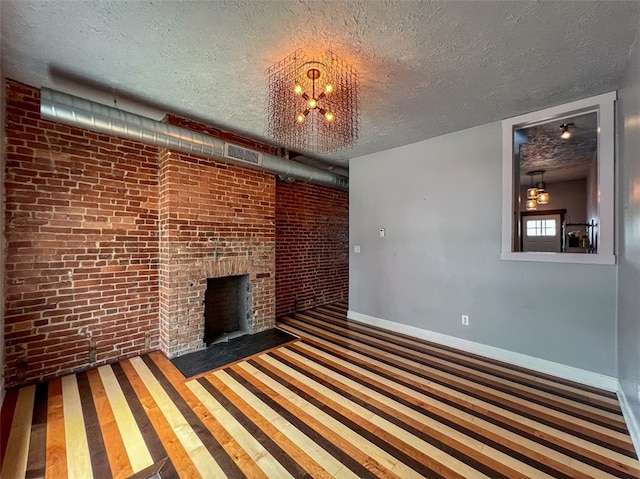 unfurnished living room with a notable chandelier, a fireplace, brick wall, and a textured ceiling