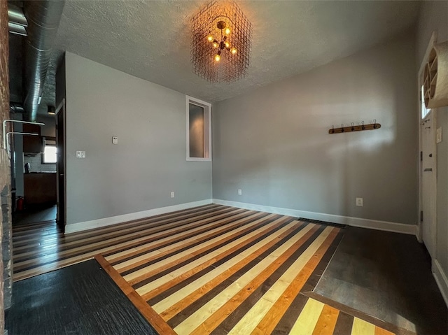 empty room featuring a textured ceiling, wood-type flooring, and a chandelier