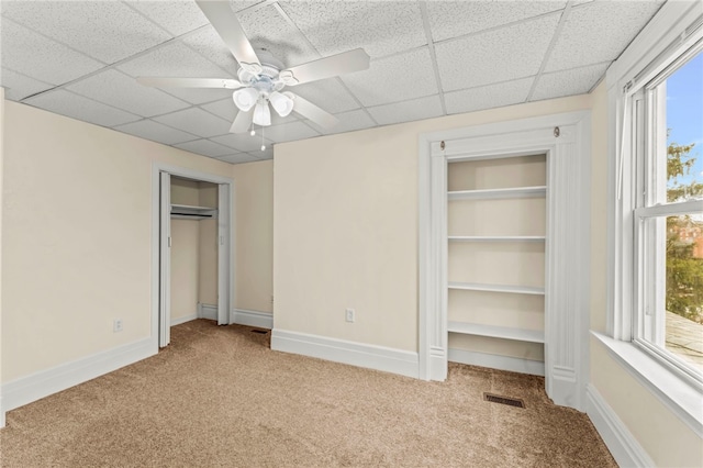 unfurnished bedroom with a paneled ceiling, carpet, multiple windows, and ceiling fan