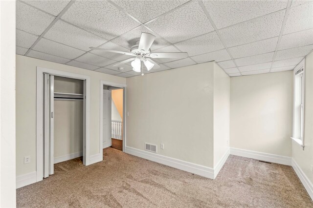 unfurnished bedroom featuring a paneled ceiling, carpet, ceiling fan, and a closet