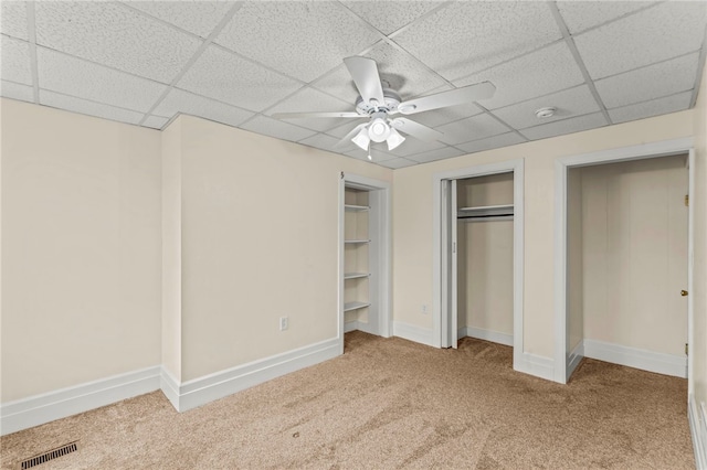 unfurnished bedroom with two closets, ceiling fan, carpet flooring, and a drop ceiling