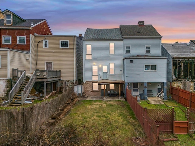 back house at dusk with a patio, a wooden deck, and a yard