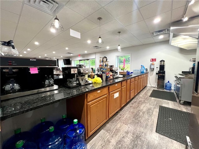 interior space with a drop ceiling, decorative light fixtures, light wood-type flooring, and dark stone countertops