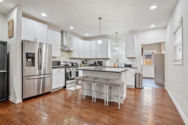 kitchen featuring a kitchen bar, a kitchen island, tasteful backsplash, stainless steel appliances, and wall chimney exhaust hood