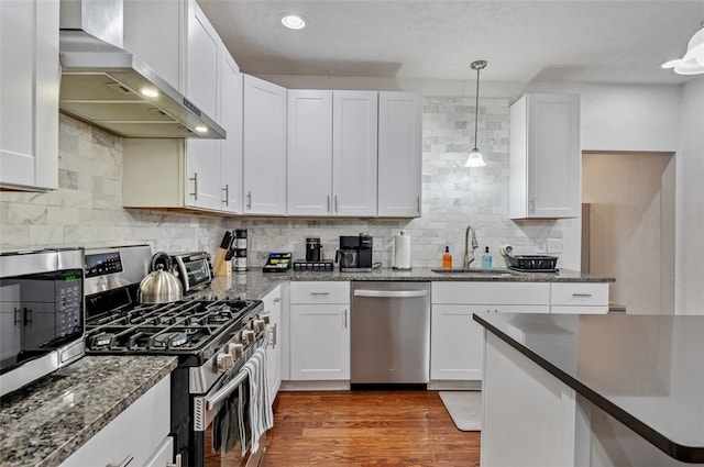 kitchen featuring stainless steel appliances, wood finished floors, white cabinetry, wall chimney exhaust hood, and a sink