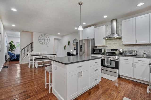 kitchen featuring dark countertops, wall chimney exhaust hood, visible vents, and appliances with stainless steel finishes