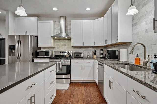 kitchen featuring tasteful backsplash, dark wood finished floors, appliances with stainless steel finishes, wall chimney exhaust hood, and a sink