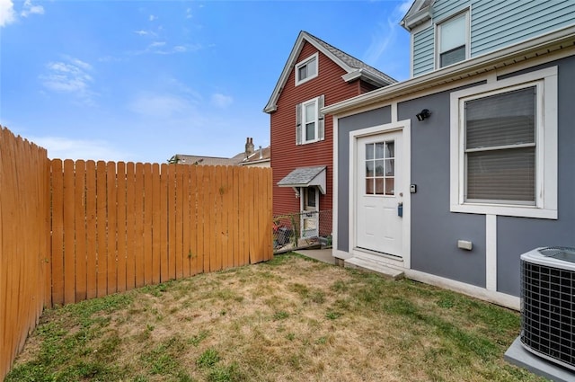 doorway to property with stucco siding, central AC unit, a yard, and fence