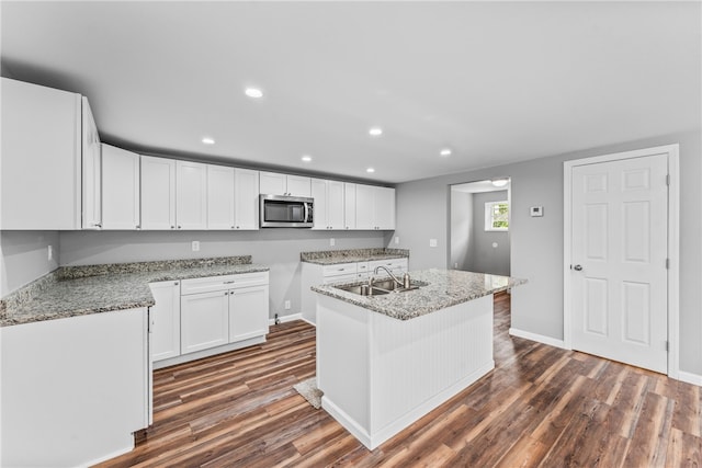 kitchen featuring white cabinetry, sink, light stone countertops, a center island with sink, and dark wood-type flooring