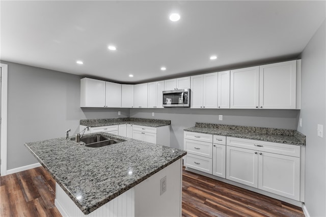 kitchen with sink, white cabinetry, light stone counters, and dark wood-type flooring