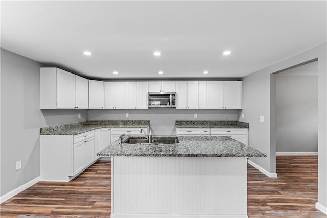 kitchen with white cabinetry, sink, light stone counters, dark hardwood / wood-style floors, and a kitchen island with sink