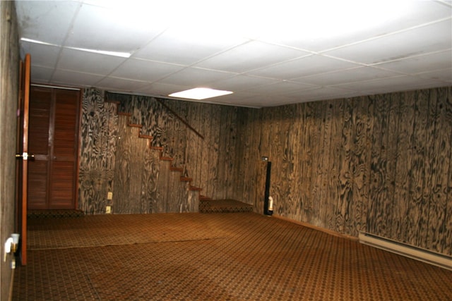 basement featuring wood walls, carpet floors, and a baseboard heating unit