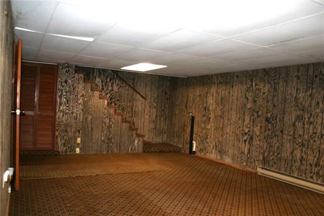 finished basement with stairway, a paneled ceiling, wooden walls, and carpet flooring