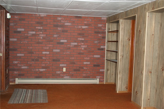 carpeted spare room featuring a drop ceiling, a baseboard heating unit, and wood walls