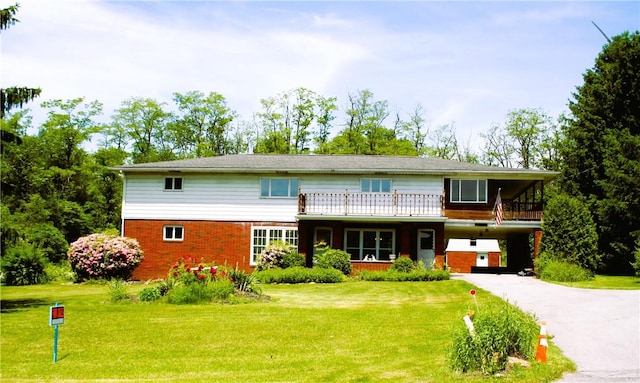 view of front of property with aphalt driveway, a carport, brick siding, and a front lawn