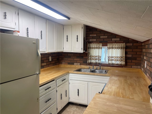 kitchen featuring white cabinetry, white fridge, brick wall, sink, and butcher block countertops