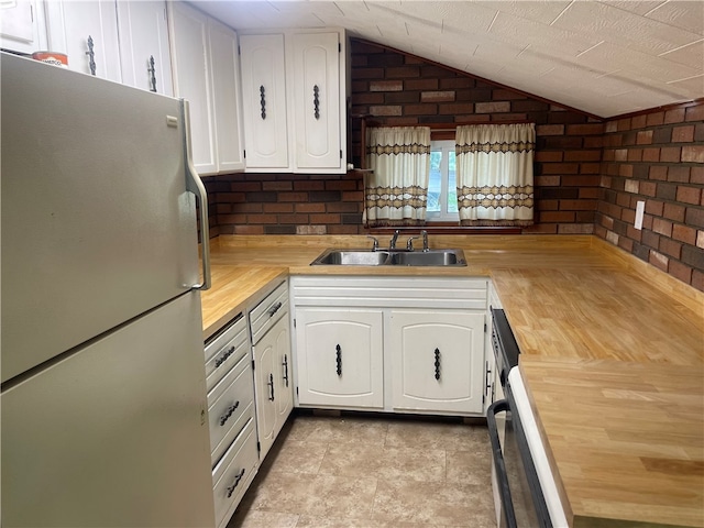 kitchen featuring white fridge, white cabinets, brick wall, sink, and light tile patterned floors