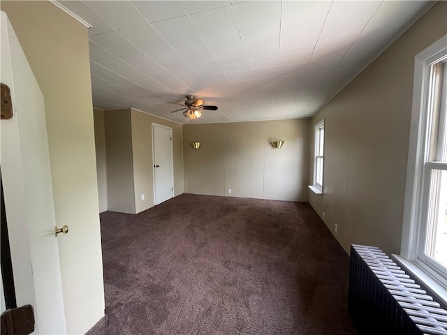 spare room with dark carpet, ceiling fan, and radiator