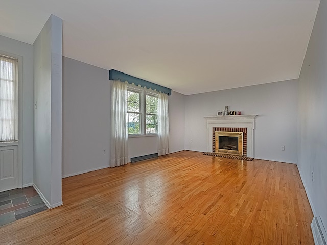 unfurnished living room featuring wood-type flooring, a fireplace, and a baseboard heating unit