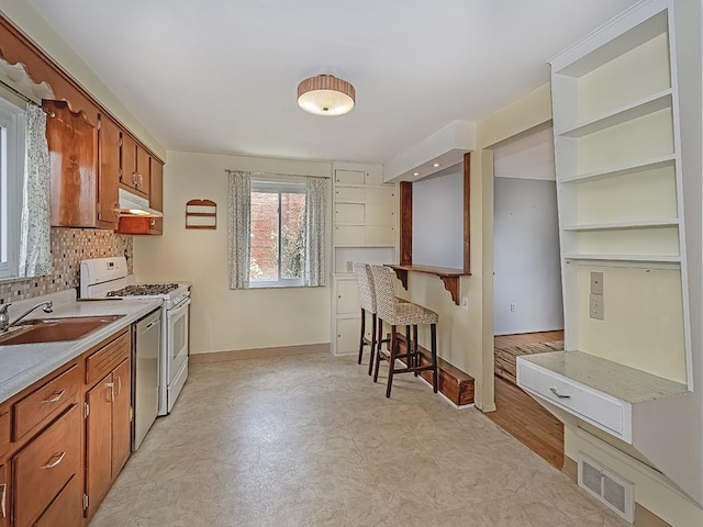 kitchen with backsplash, white range, sink, dishwasher, and a breakfast bar area