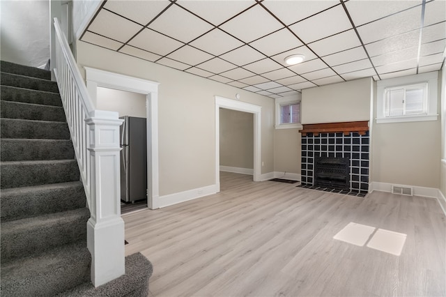 unfurnished living room with a paneled ceiling, a tiled fireplace, and light wood-type flooring