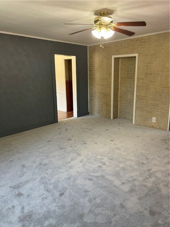 carpeted empty room with ceiling fan, brick wall, and crown molding