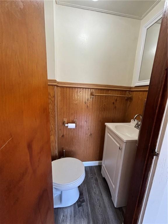 bathroom with wood-type flooring, wooden walls, vanity, and toilet