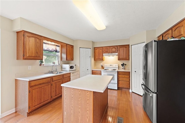 kitchen featuring sink, a center island, light hardwood / wood-style flooring, a textured ceiling, and white appliances